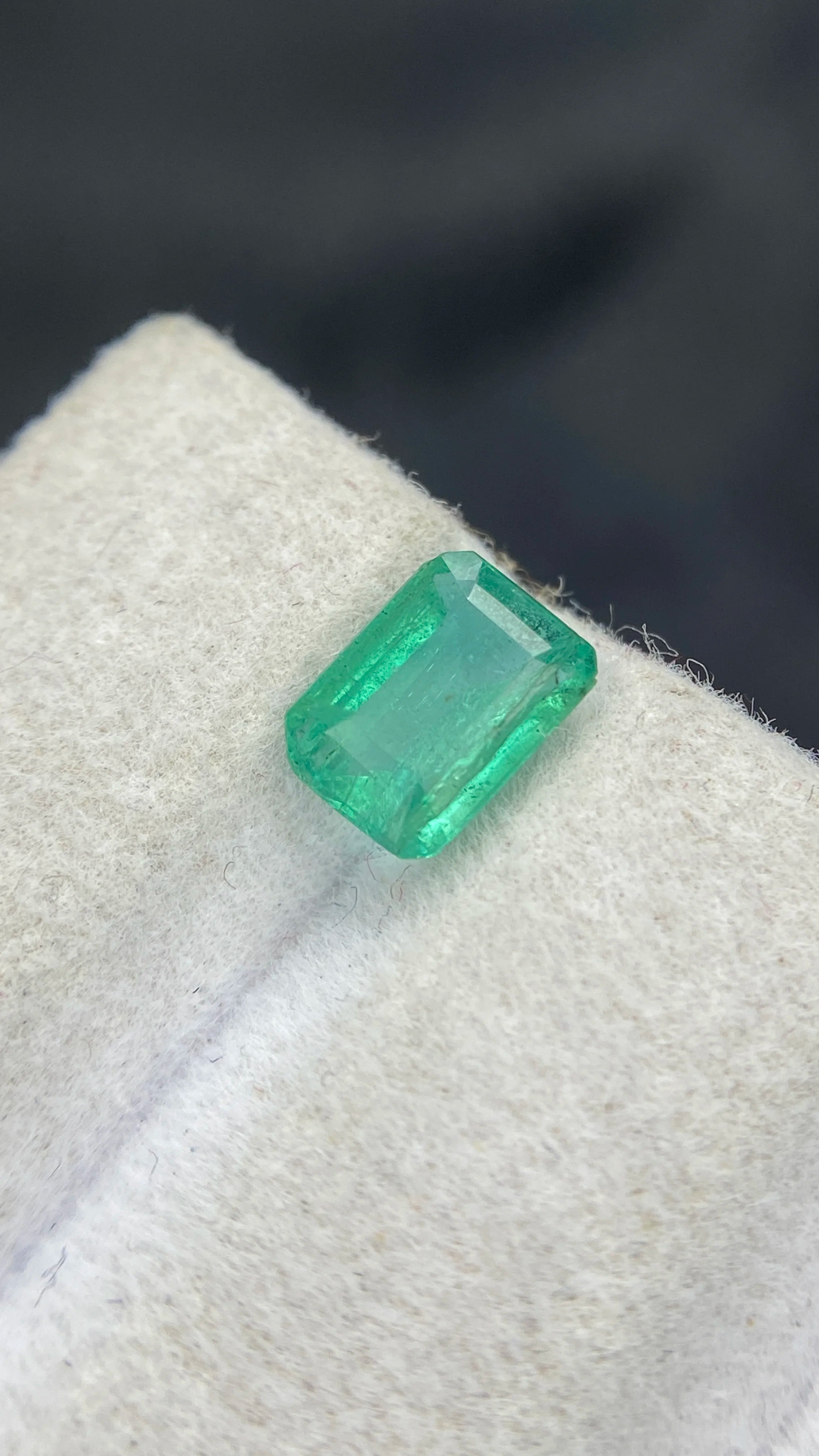 Loose emerald-cut green gemstone, small close-up on white felt pad