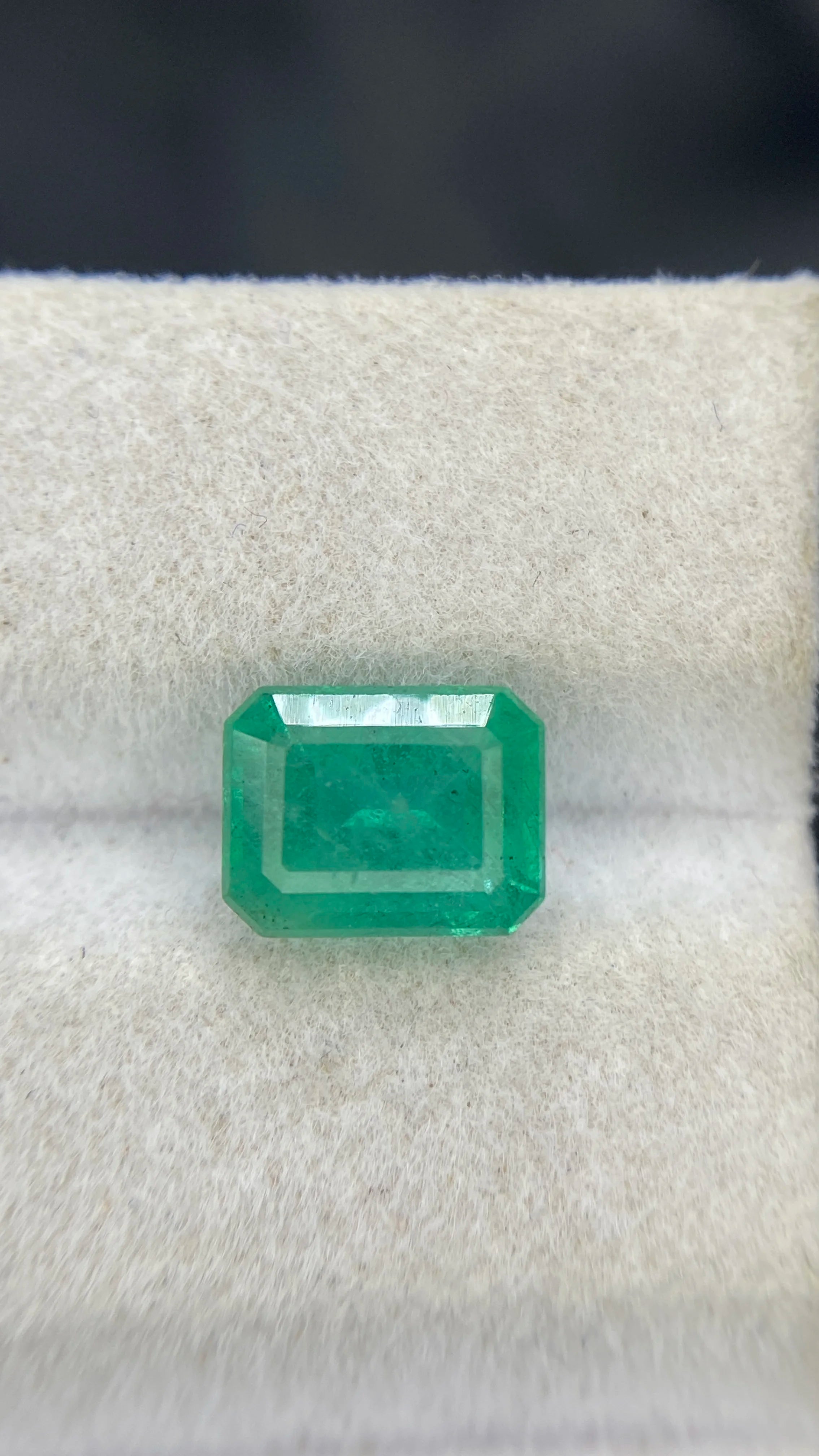 Emerald-cut green gemstone facing view on white felt