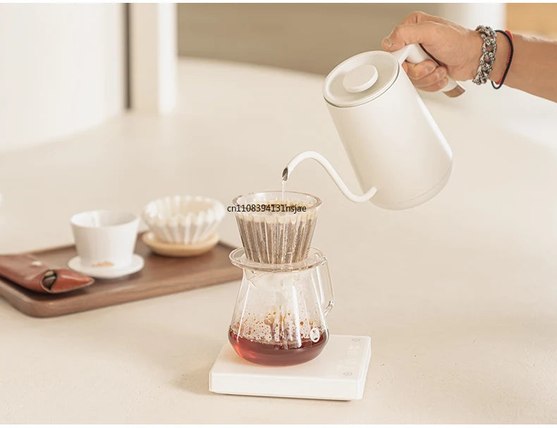 Matte white gooseneck kettle pouring hot water into a glass pour-over coffee dripper and carafe set on a scale.