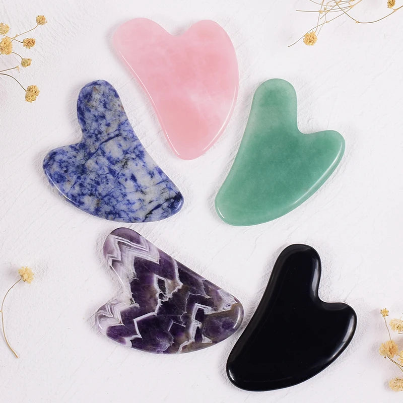 Five heart-shaped gua sha massage tools in pink, green, blue-speckled, purple-striped, and solid black stone.