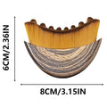 Crescent-shaped facial brush with wooden-grain handle and soft golden bristles, measuring 8cm by 6cm.