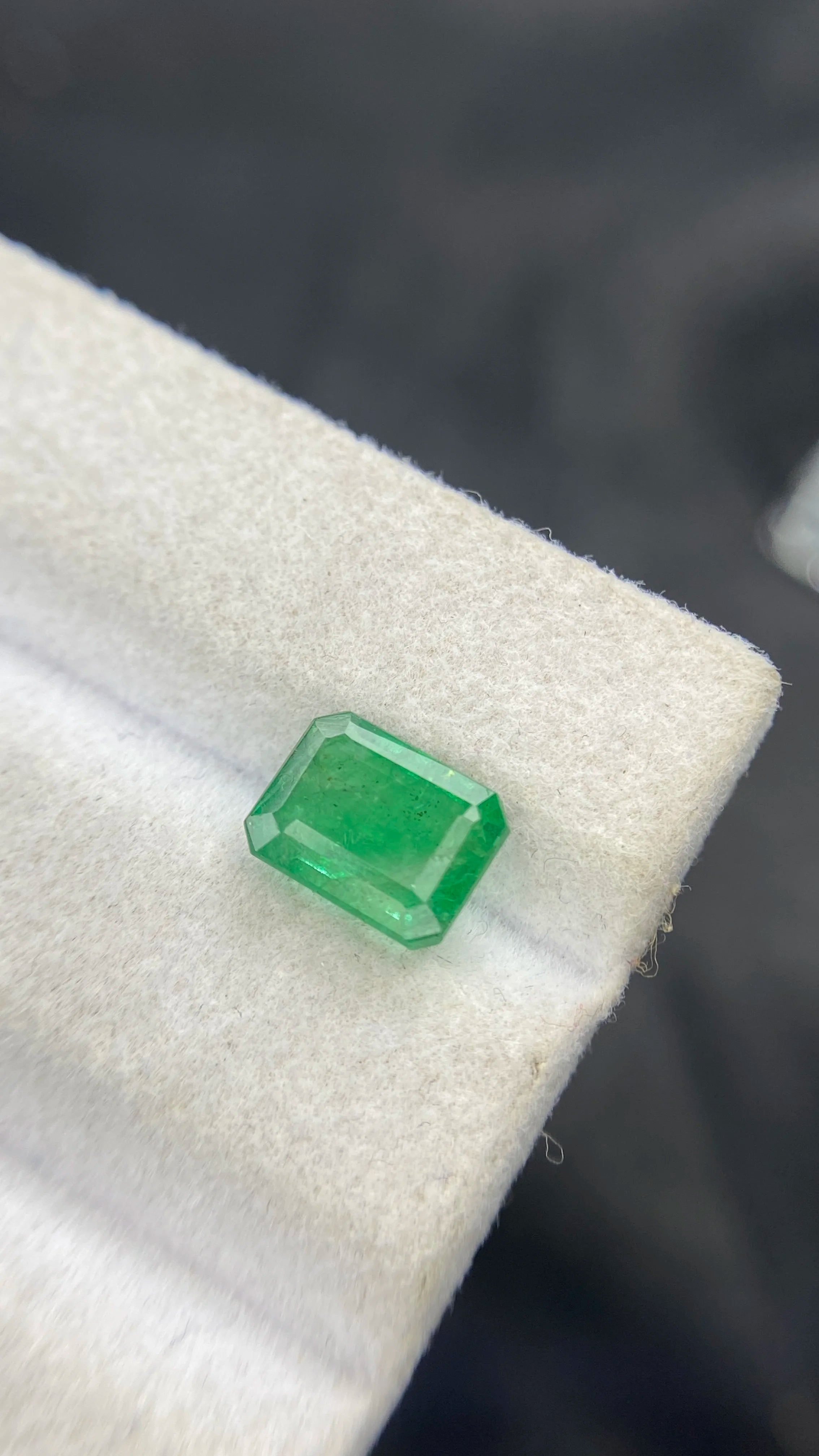Green emerald-cut loose gemstone, side view on soft light jewelry pad