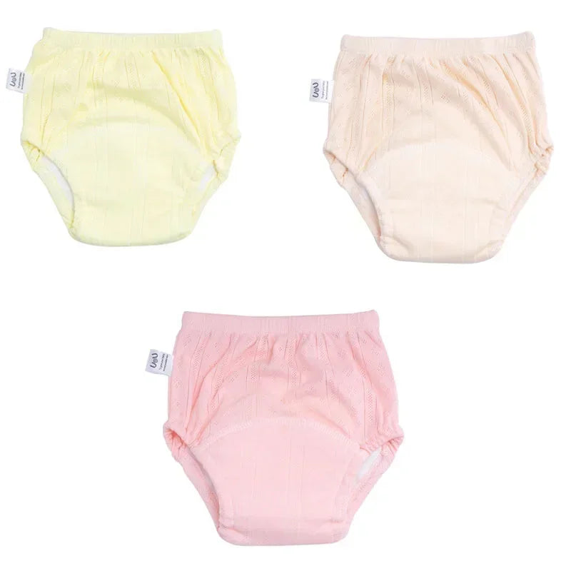Three-pack of pastel baby training diapers in yellow, cream, and pink, featuring soft cotton fabric.