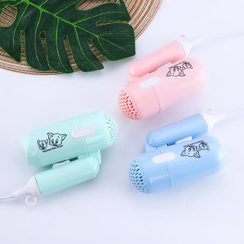 Three mini folding hair dryers in pink, blue, and mint green with cartoon designs, perfect for travel or dorm use.