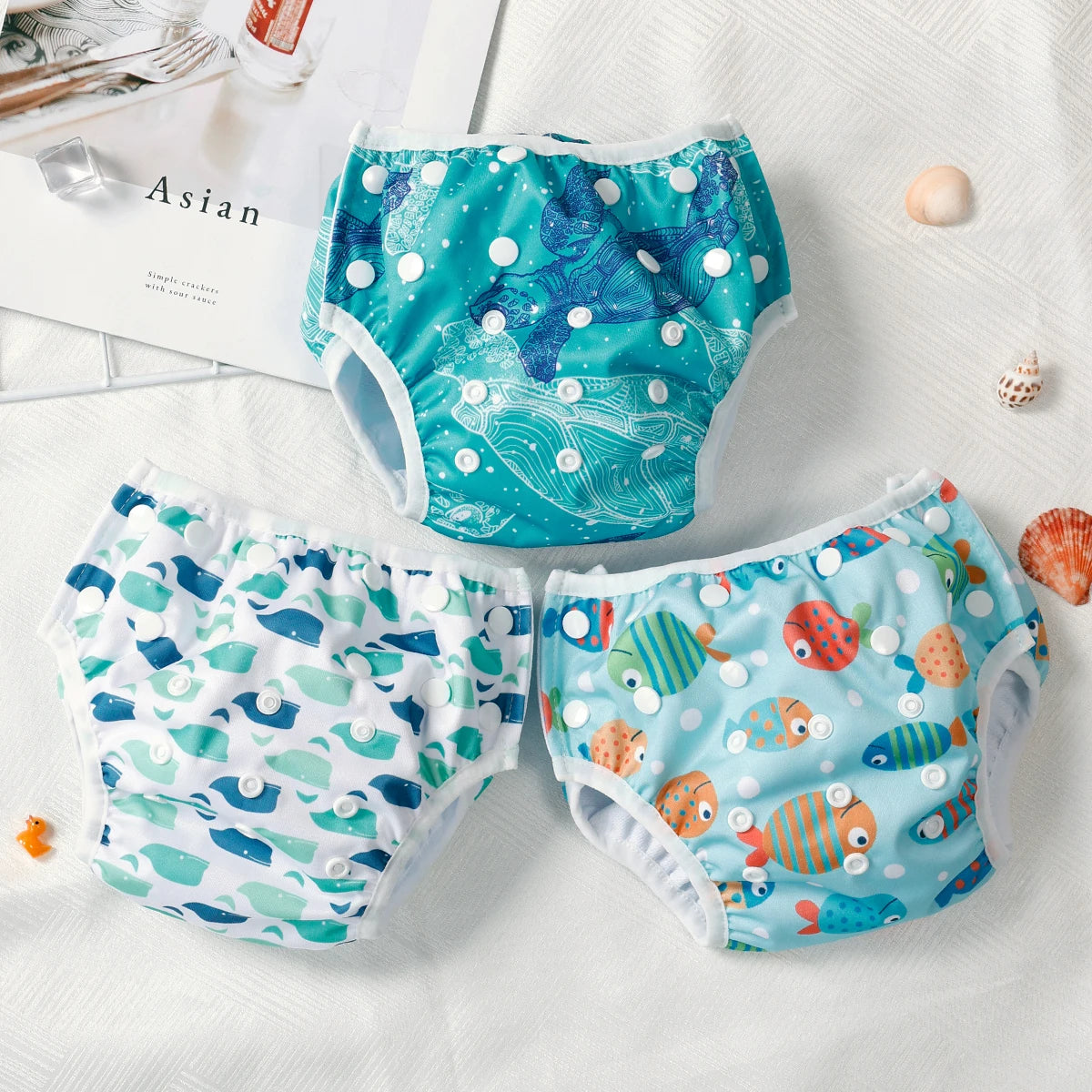 Three reusable baby swim diapers with ocean turtle, whale, and fish prints on a white background.