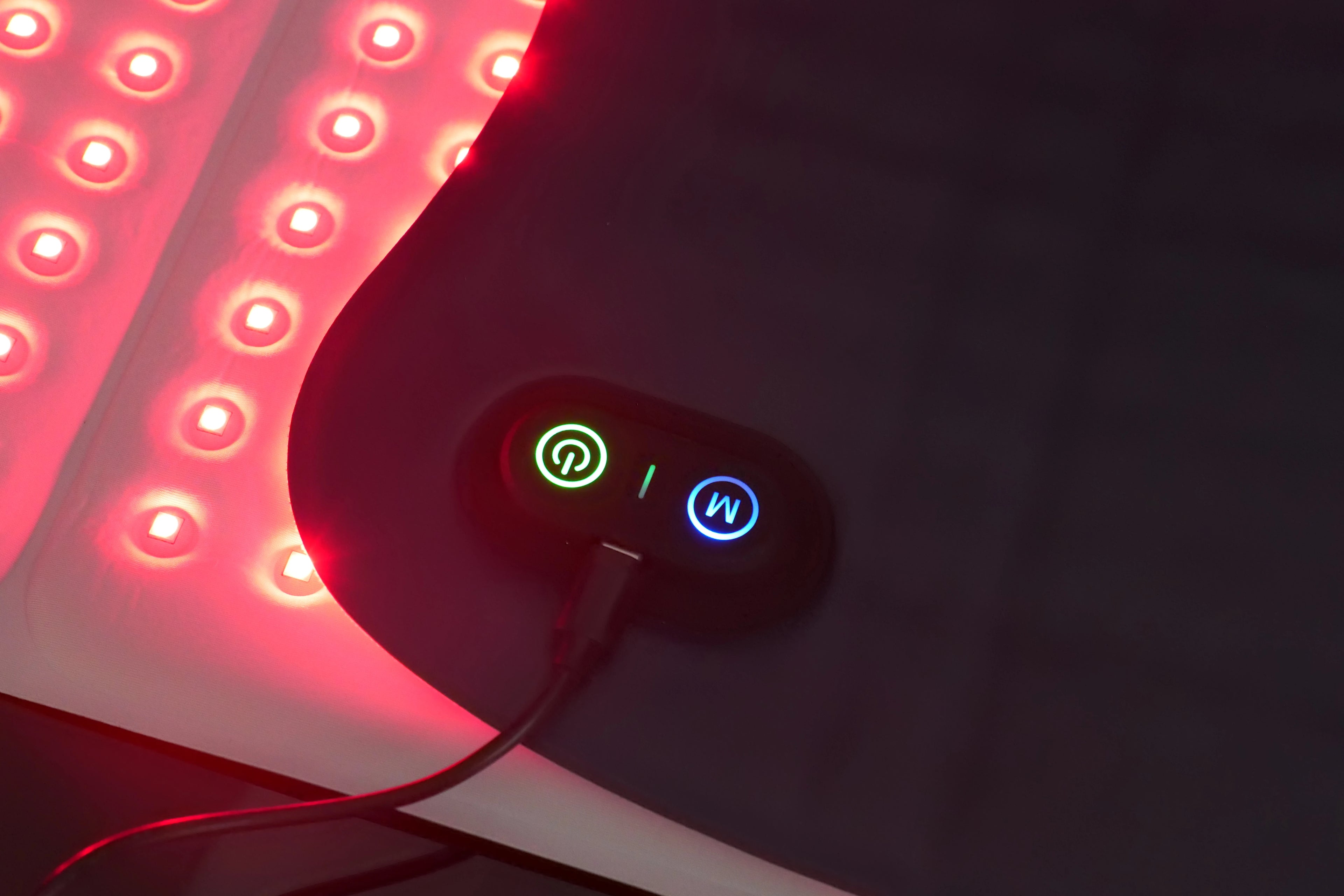 Red light therapy pad with a black flexible surface, glowing red LED diodes, and a power control panel.