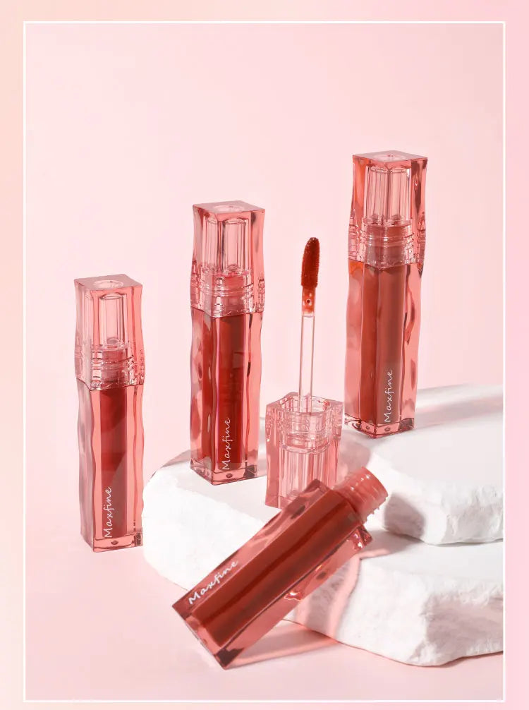 Maxfine highly pigmented moisturizing liquid lip glaze in crystal square tubes with applicator on a white stone base.