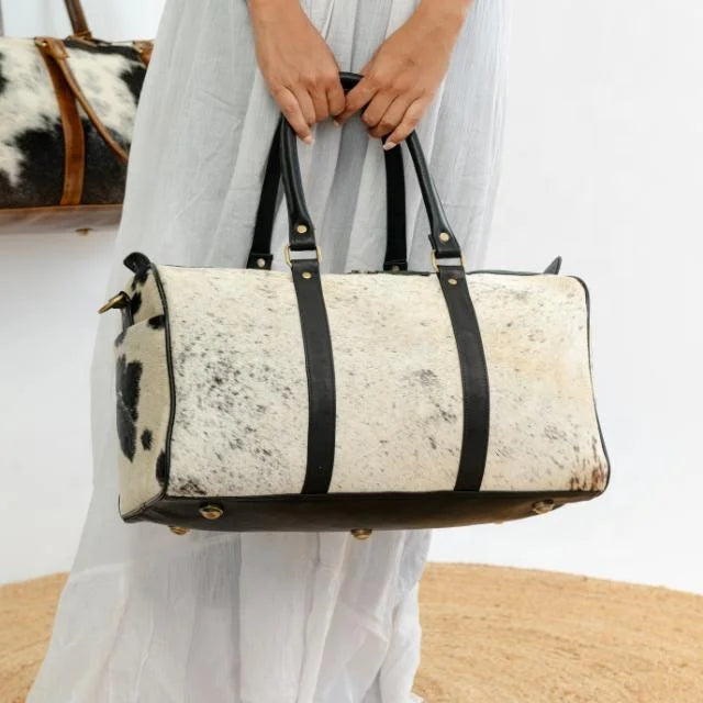 Unisex white and black cow hair-on-hide leather weekender duffel bag with black leather straps and brass hardware.