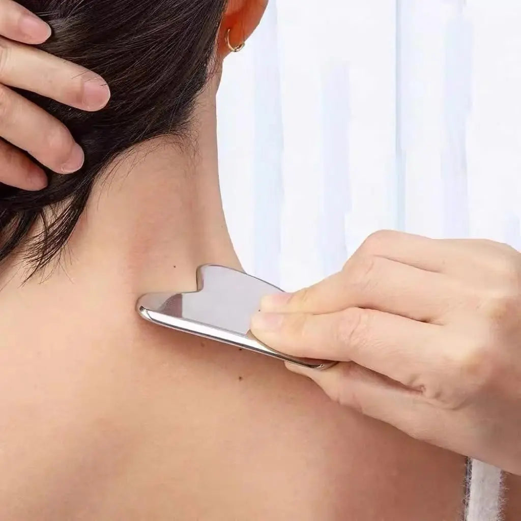 A hand uses a smooth, heart-shaped stainless steel gua sha tool to massage the side of a person’s neck.