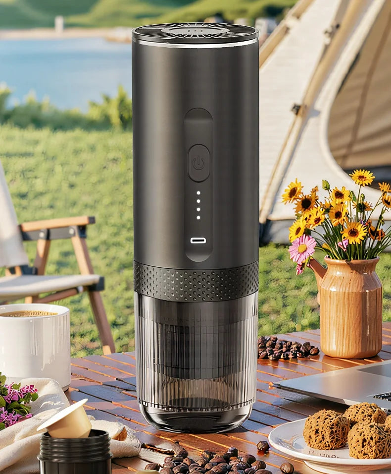 Portable black electric espresso maker with clear base on outdoor camping table, modern minimalist design.