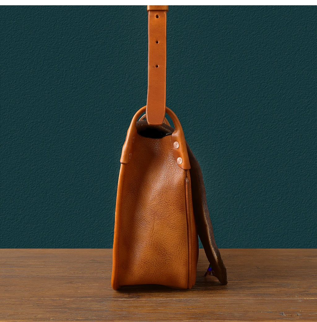Side view of a vintage tan genuine cowhide leather messenger bag with an adjustable shoulder strap and rivet detailing.