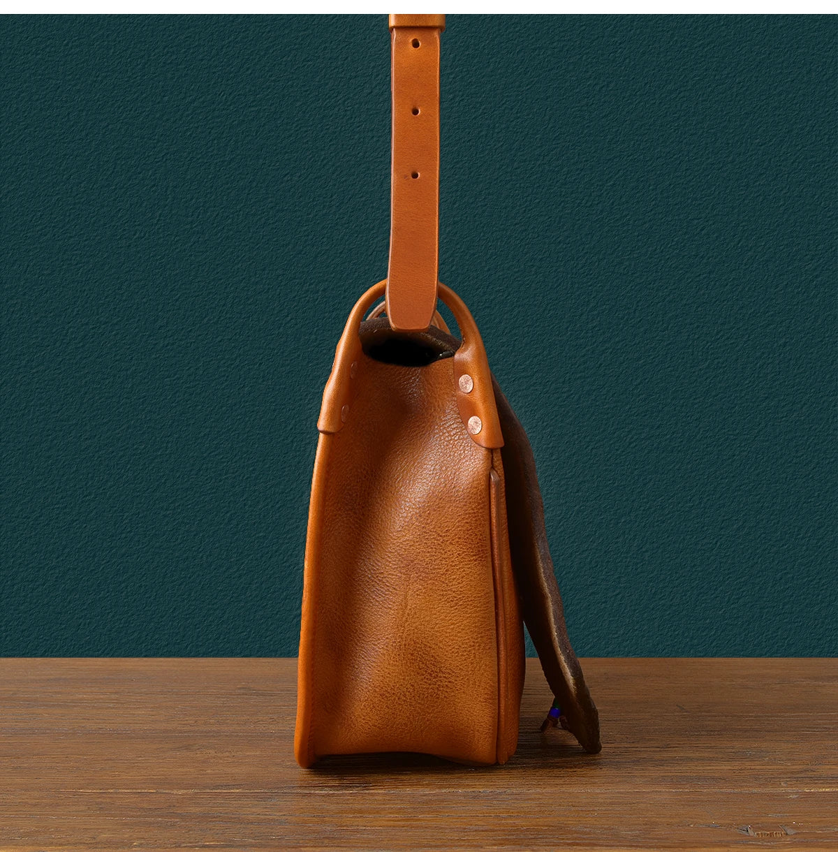 Side view of a vintage tan genuine cowhide leather messenger bag with an adjustable shoulder strap and rivet detailing.