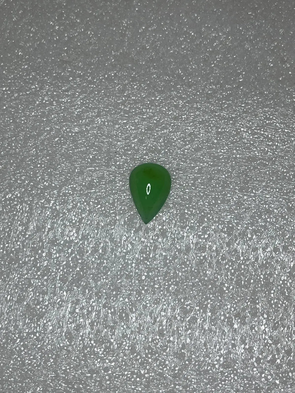 Dark green chrysoprase pear-shaped cabochon gemstone, polished teardrop on textured gray.