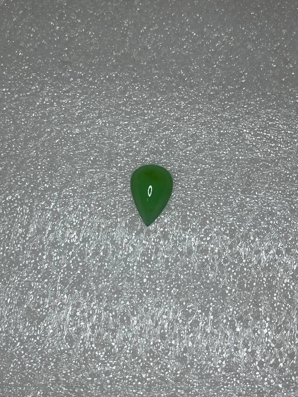 Dark green chrysoprase pear-shaped cabochon gemstone, polished teardrop on textured gray.