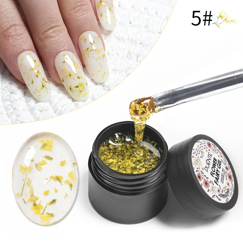 Clear gel nail polish with small dried yellow flowers in a black jar, applied to fingernails with a brush.