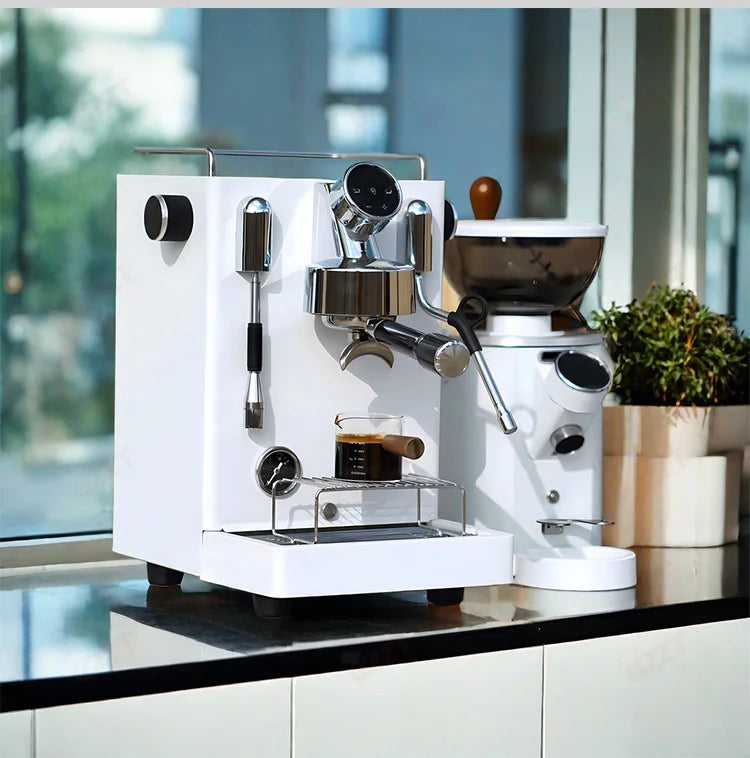 Modern white espresso machine and matching coffee grinder on a kitchen counter with chrome details and pressure gauge.