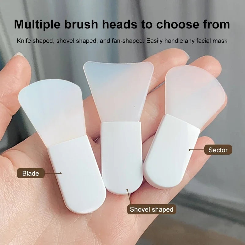 Three small white silicone facial mask applicators with different brush head shapes held in a palm.