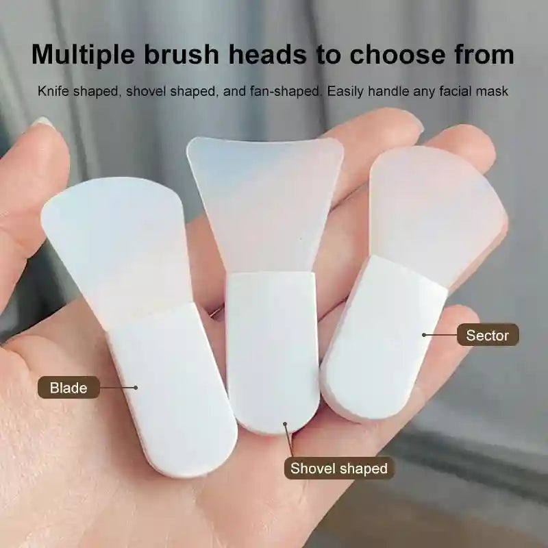 Three silicone facial mask brushes with white handles and translucent, differently shaped heads held in a hand.