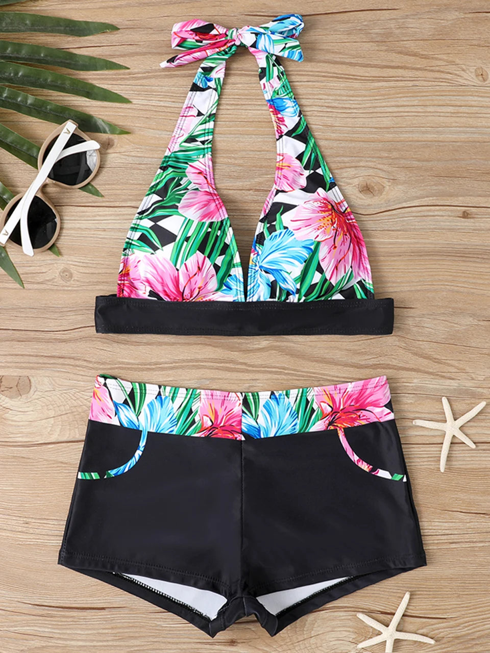 Tidesmit high-waist bikini featuring a black and colorful tropical floral print on a wood background.