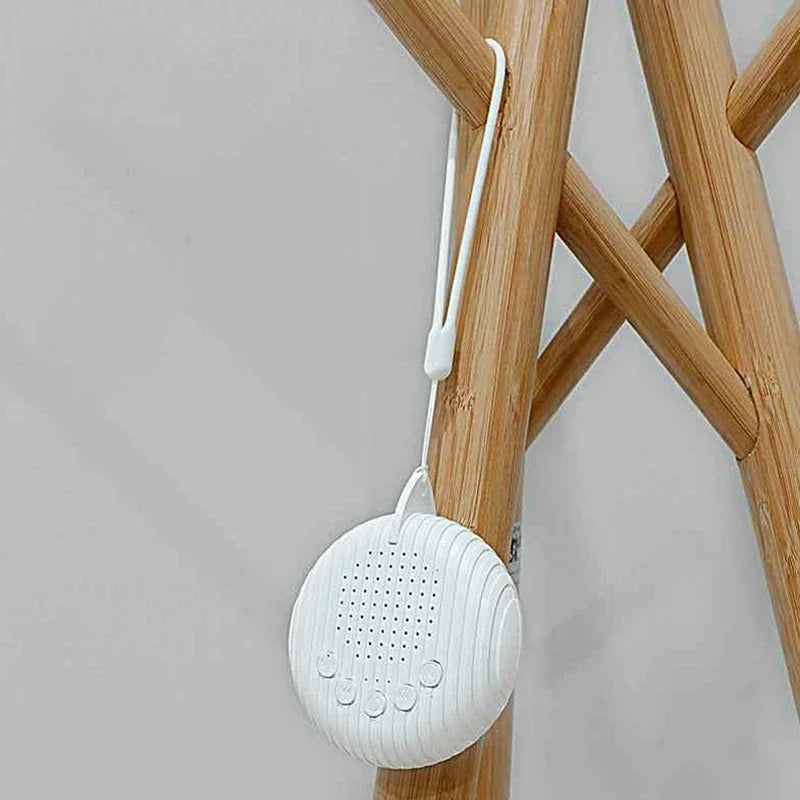 Small white portable sound machine for better sleep with visible control buttons, hanging on a wooden stand.