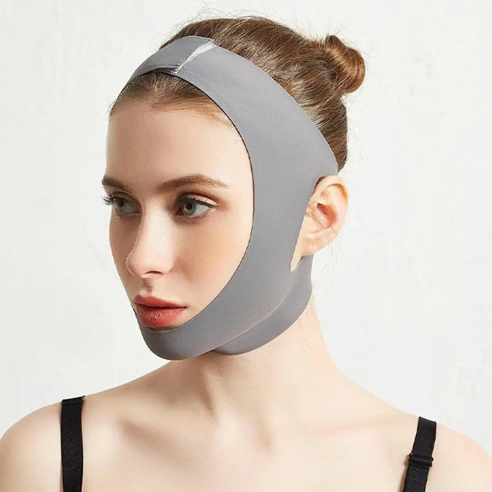 A woman wearing a gray, smooth, fabric V-line face shaper mask that supports the chin and wraps around the head.
