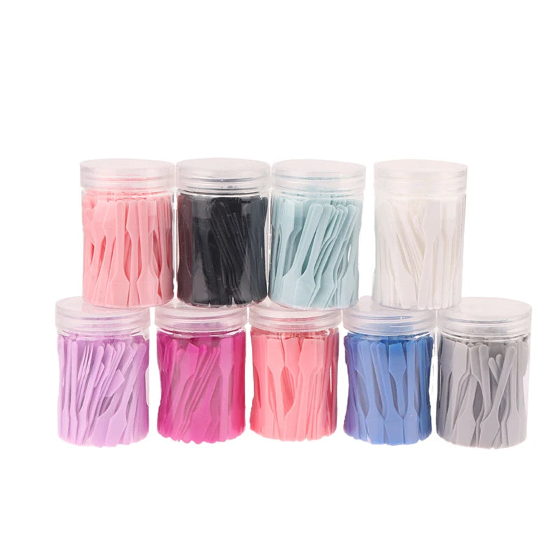 Nine clear plastic jars filled with small, colorful mini cosmetic spatulas in various pastel and solid colors.