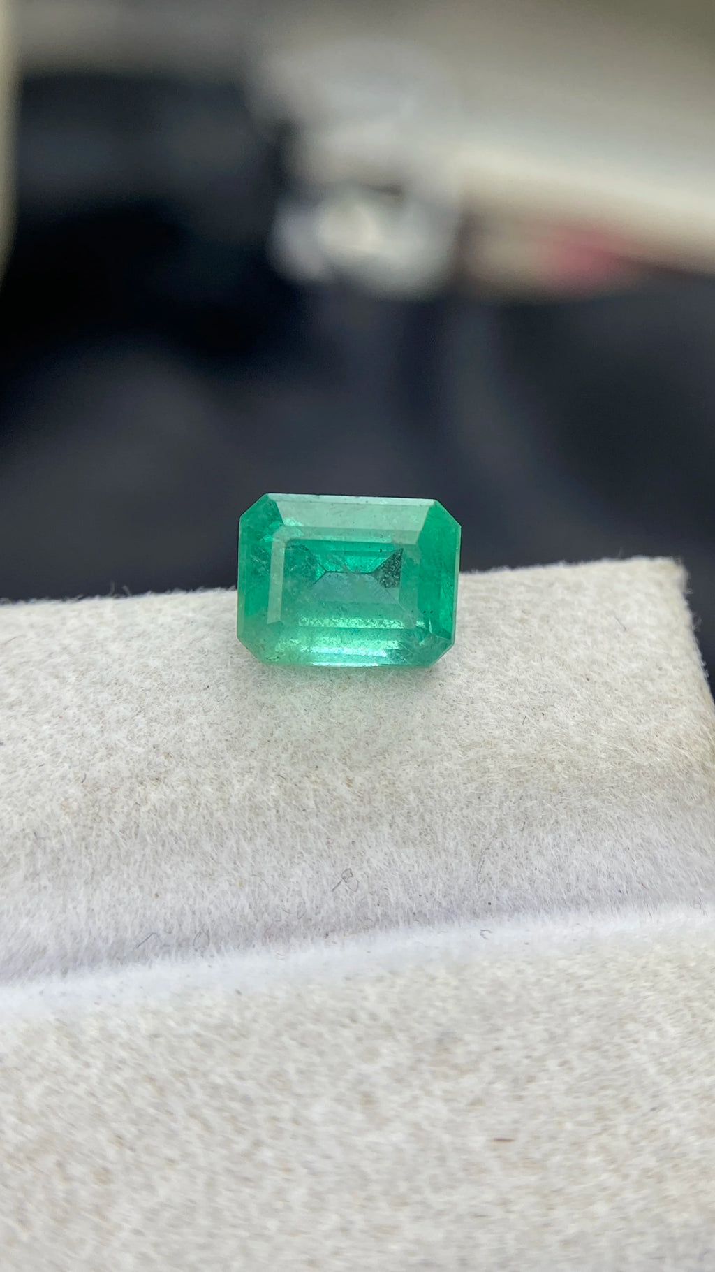 Emerald-cut green gemstone with step facets on white felt