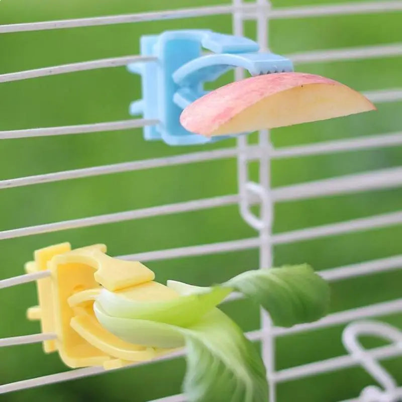 Blue and yellow plastic bird food clips holding fruit and vegetables on a cage to feed parrots and pet birds.