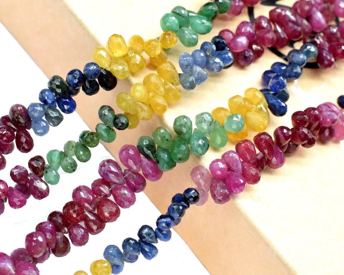 Multi-color faceted drop beads (4x6mm) arranged on a skin-tone display surface