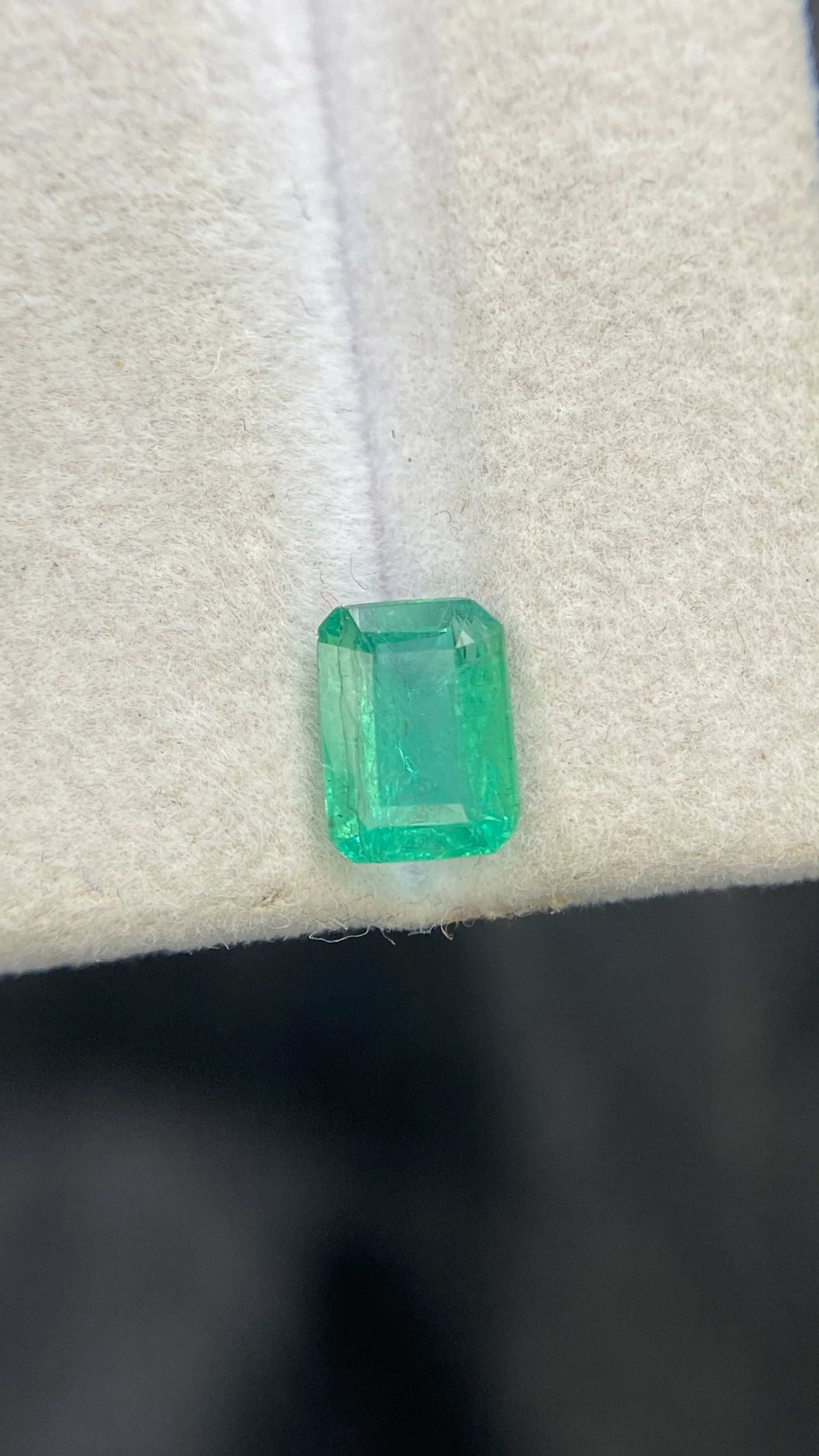Loose emerald-cut green gemstone, top view on white felt pad