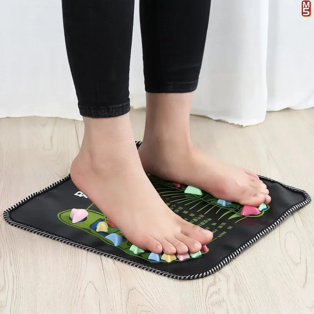 Person standing on a black reflexology acupressure massage pad with colorful pressure points for foot health care.