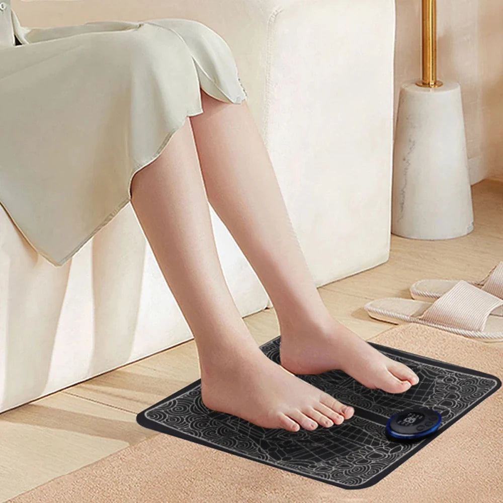Rechargeable EMS foot massage mat with digital controller for sore feet relief, shown in use on a home floor.