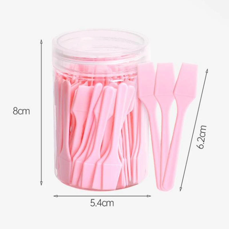 A clear jar filled with 100 small, pink, plastic cosmetic spatulas for applying face cream or makeup masks.