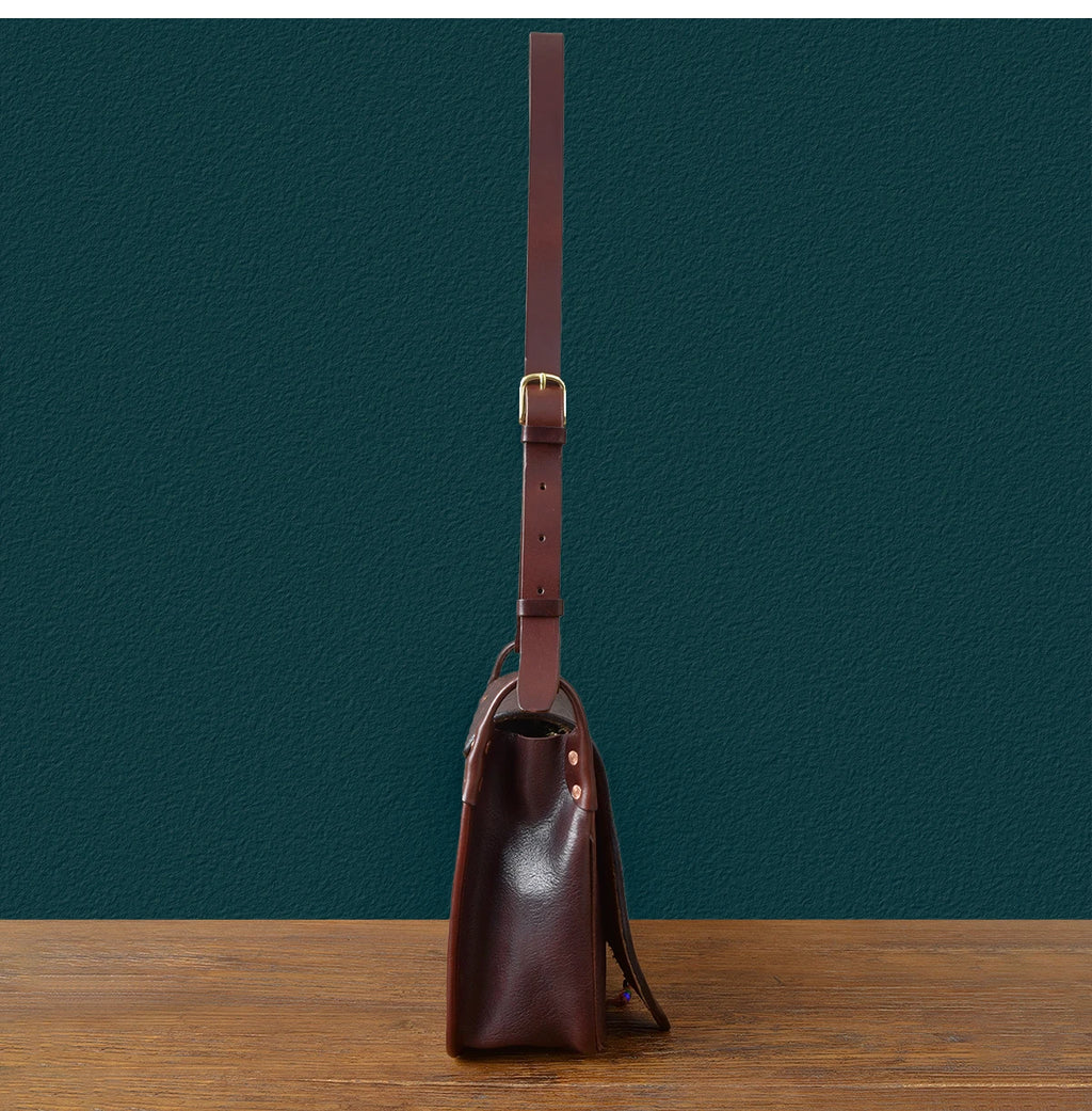 Side view of a vintage handmade dark brown cowhide messenger bag with an adjustable leather shoulder strap.
