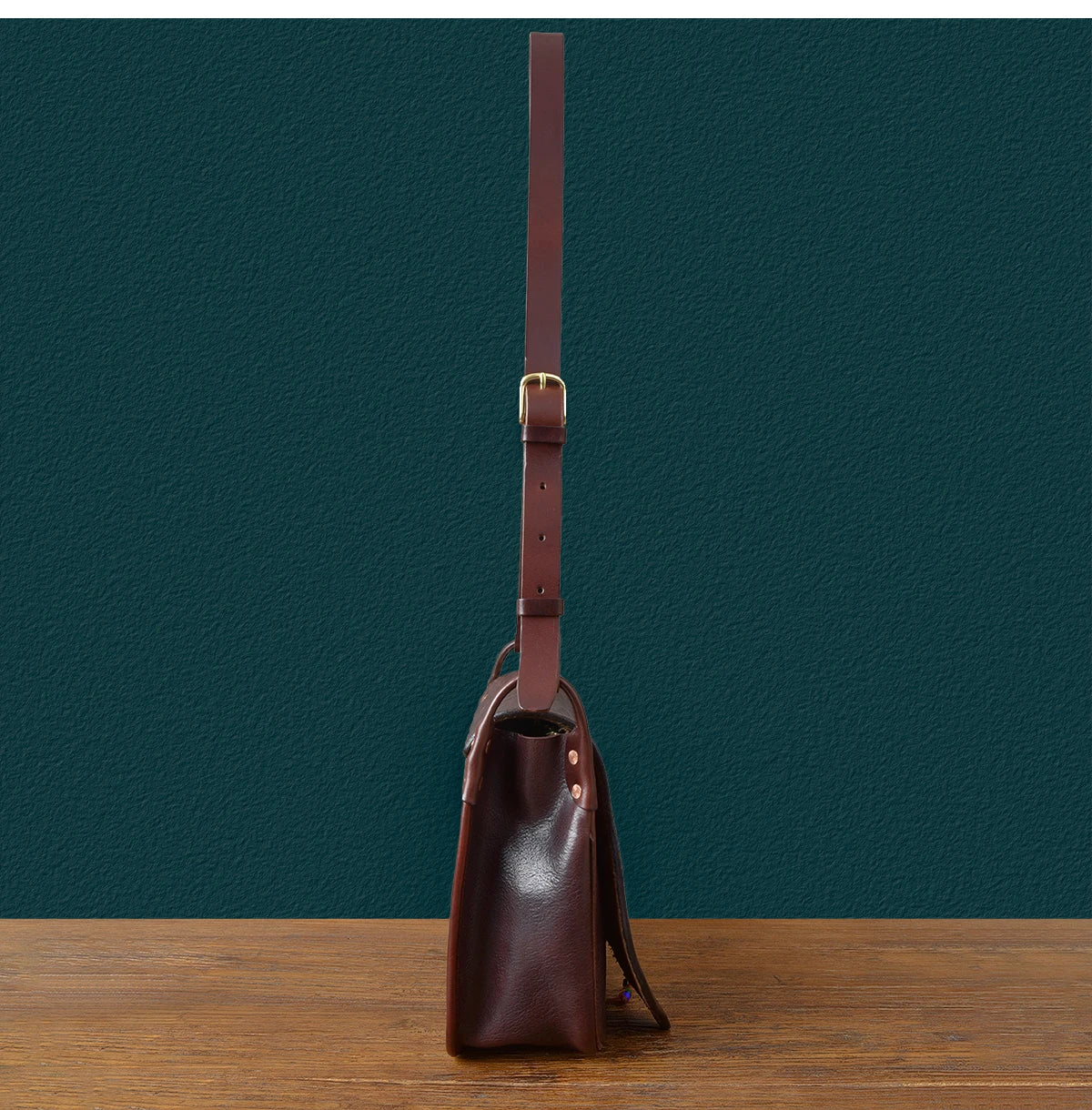 Side view of a vintage handmade dark brown cowhide messenger bag with an adjustable leather shoulder strap.