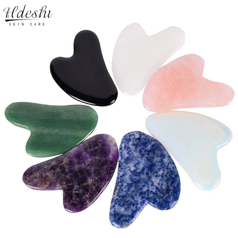 A circular arrangement of seven heart-shaped gua sha massage tools in various colors, stones, and textures.