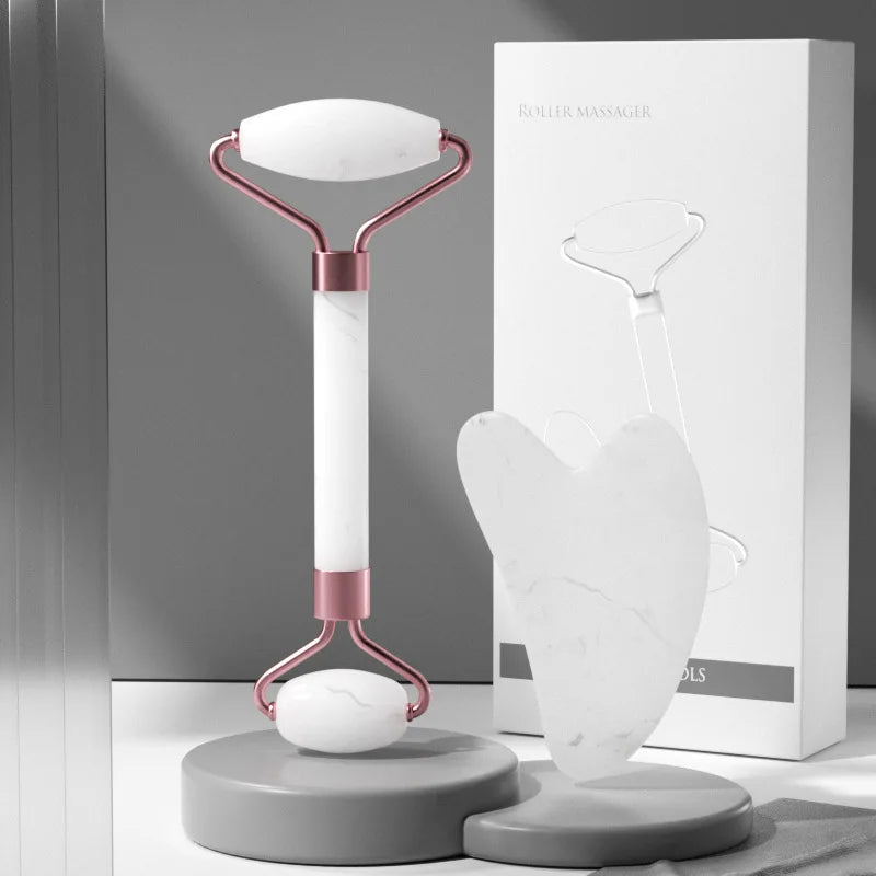 White marble facial roller with rose gold accents and a heart-shaped gua sha tool beside their product box.
