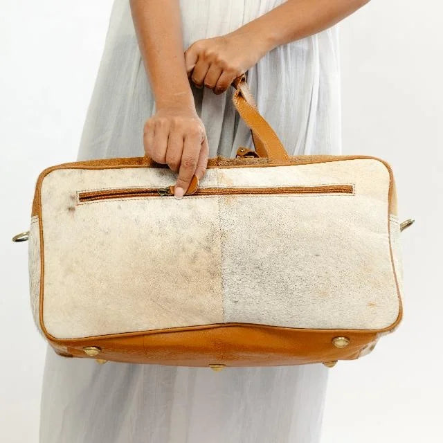 Western-style tan leather and hair-on-hide travel trunk duffel bag with zip pocket and brass feet.