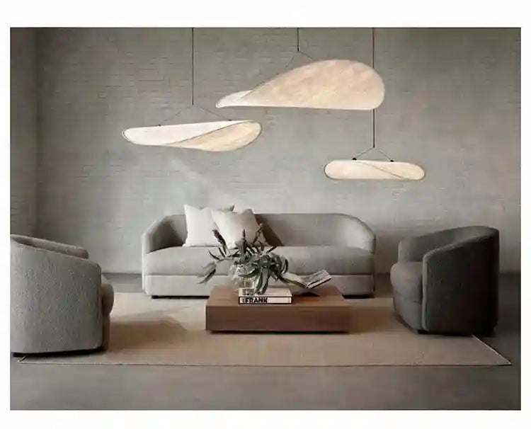 Three beige, wavy pendant lights hanging over a gray living room set, providing soft, warm overhead ambient lighting.