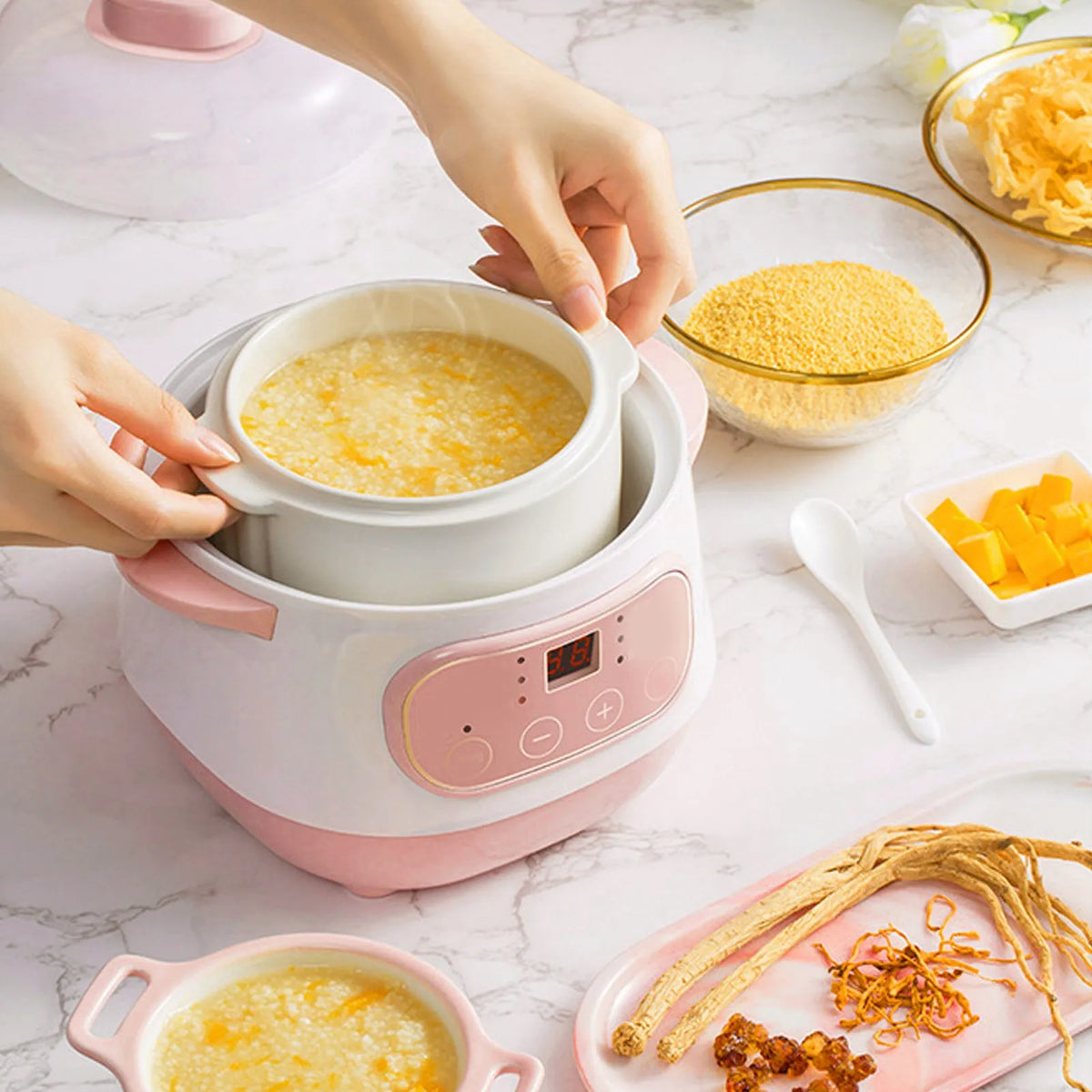 Pink mini electric rice cooker with ceramic inner pot, lid open with porridge cooking