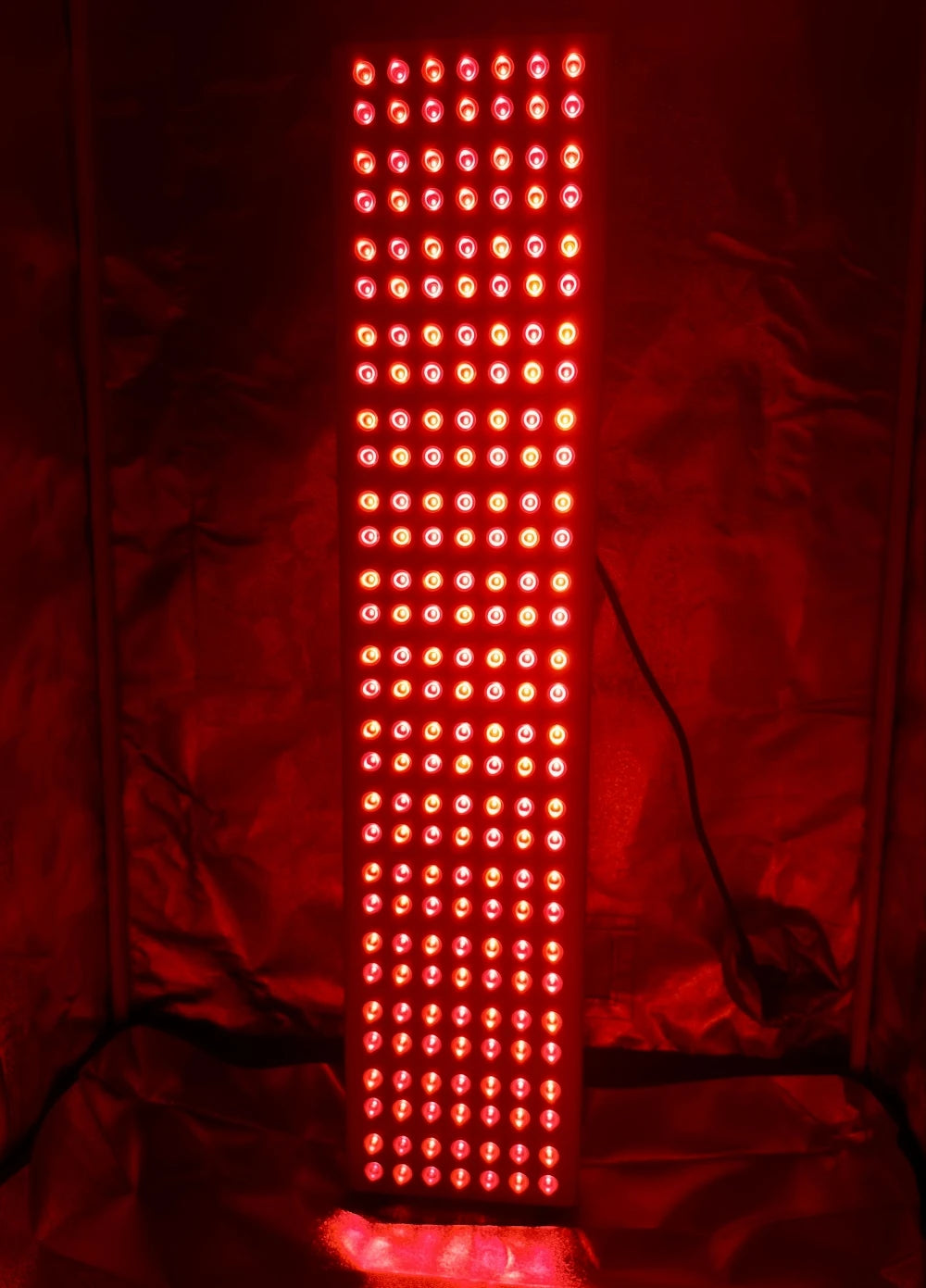 Tall red light therapy panel with LED grid for skin rejuvenation and pain relief against reflective backdrop.