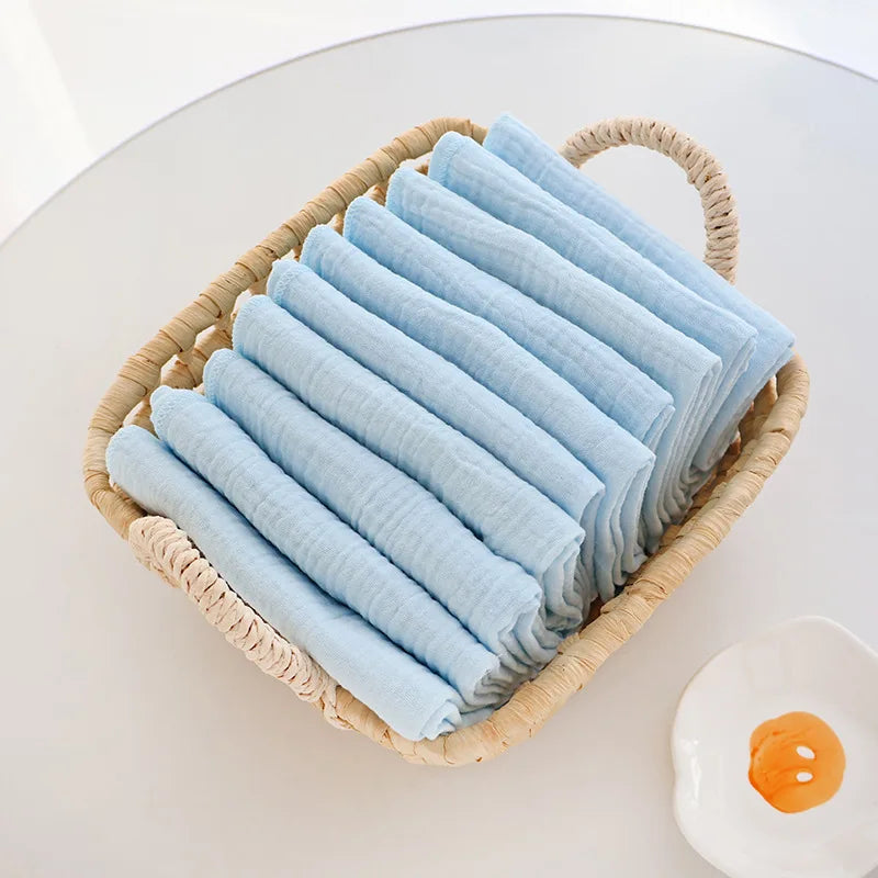 Soft blue muslin baby care washcloths folded in a woven wicker basket for gentle newborn skin care.