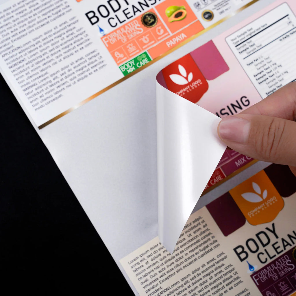 Sheet of printed adhesive labels with body care branding, partially peeled by hand.