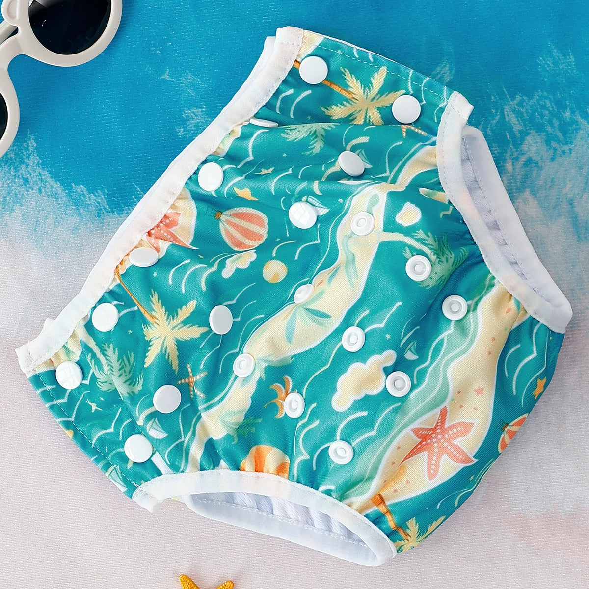 Reusable baby swim diaper with adjustable snaps, featuring a teal tropical beach and starfish print.