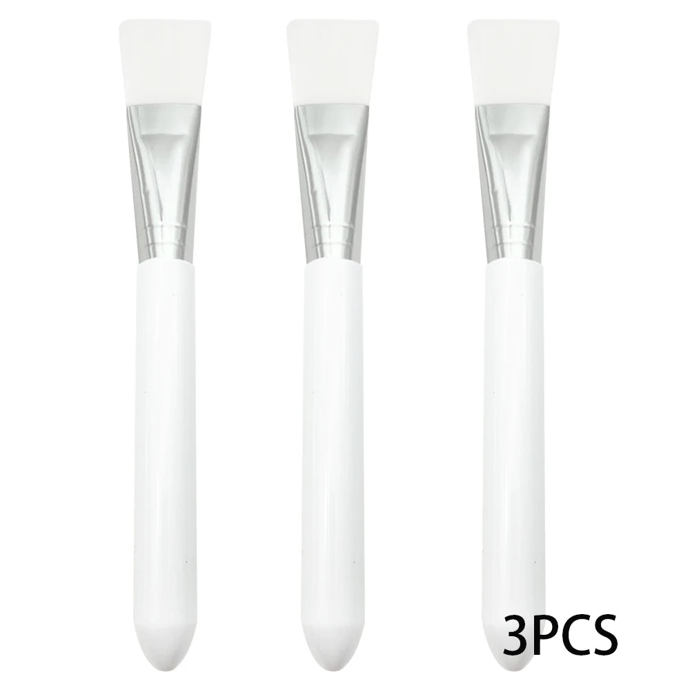 Three face mask applicator brushes with flat white silicone tips, silver metal ferrules, and white handles.