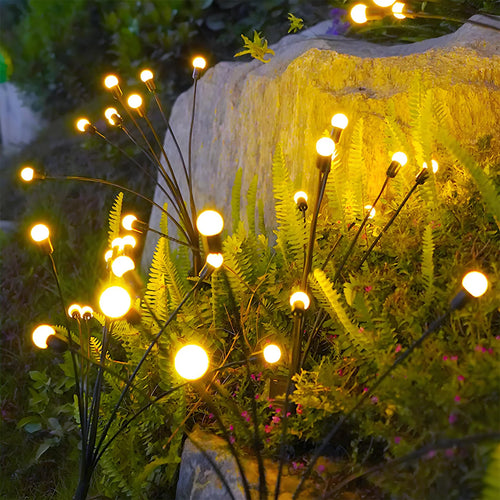 Solar firefly garden lights with black stems and glowing warm-yellow LED bulbs installed in a garden.