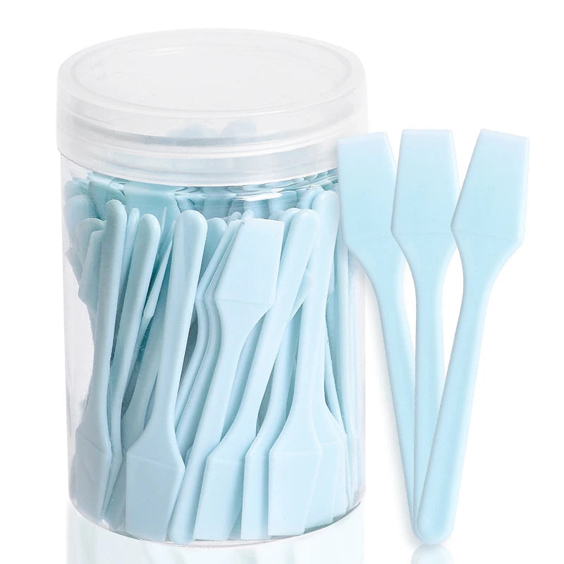 A jar filled with 100 light blue mini plastic cosmetic spatulas for applying creams and masks.