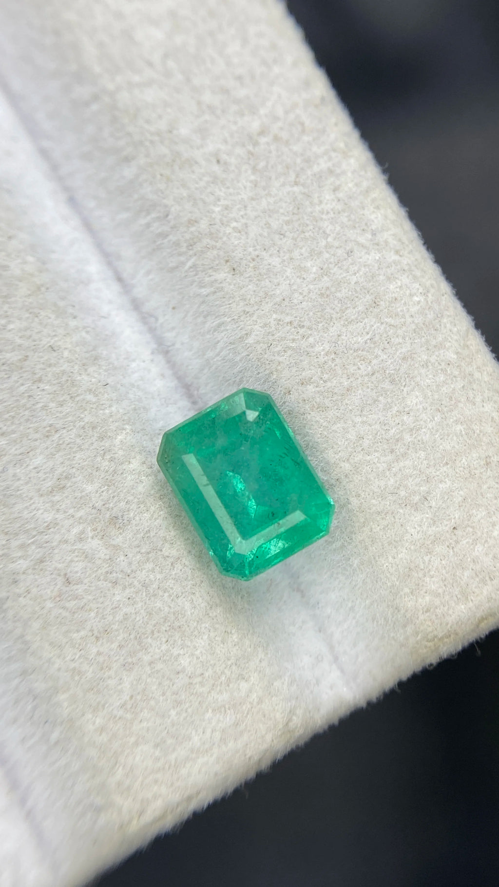 Close-up of emerald-cut green gemstone on white felt