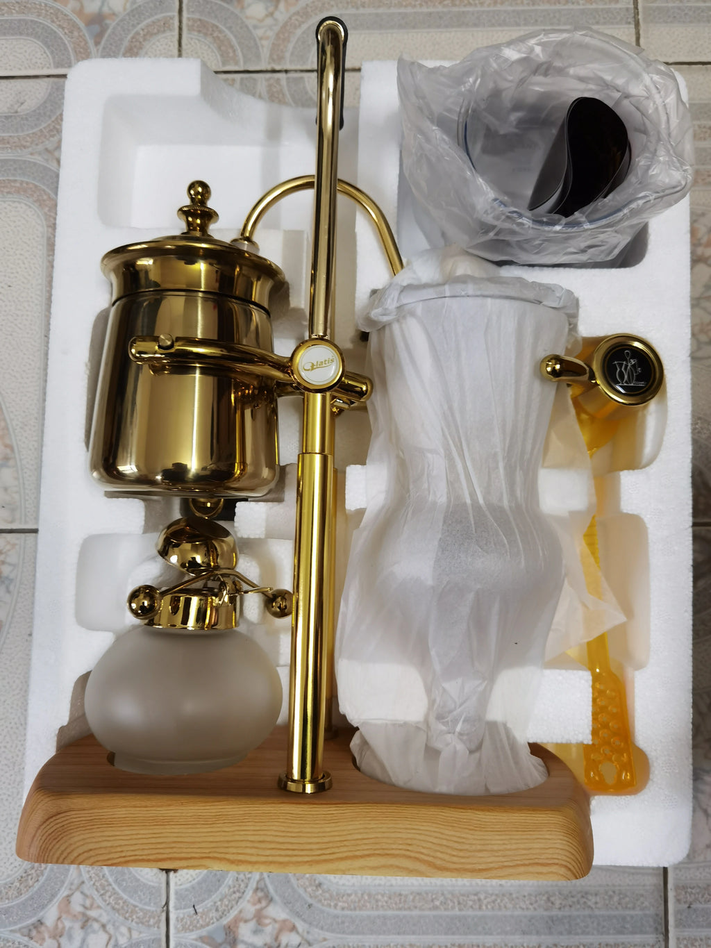 Gold Yatis balance siphon coffee maker with wooden base and frosted glass in white foam protective packaging.