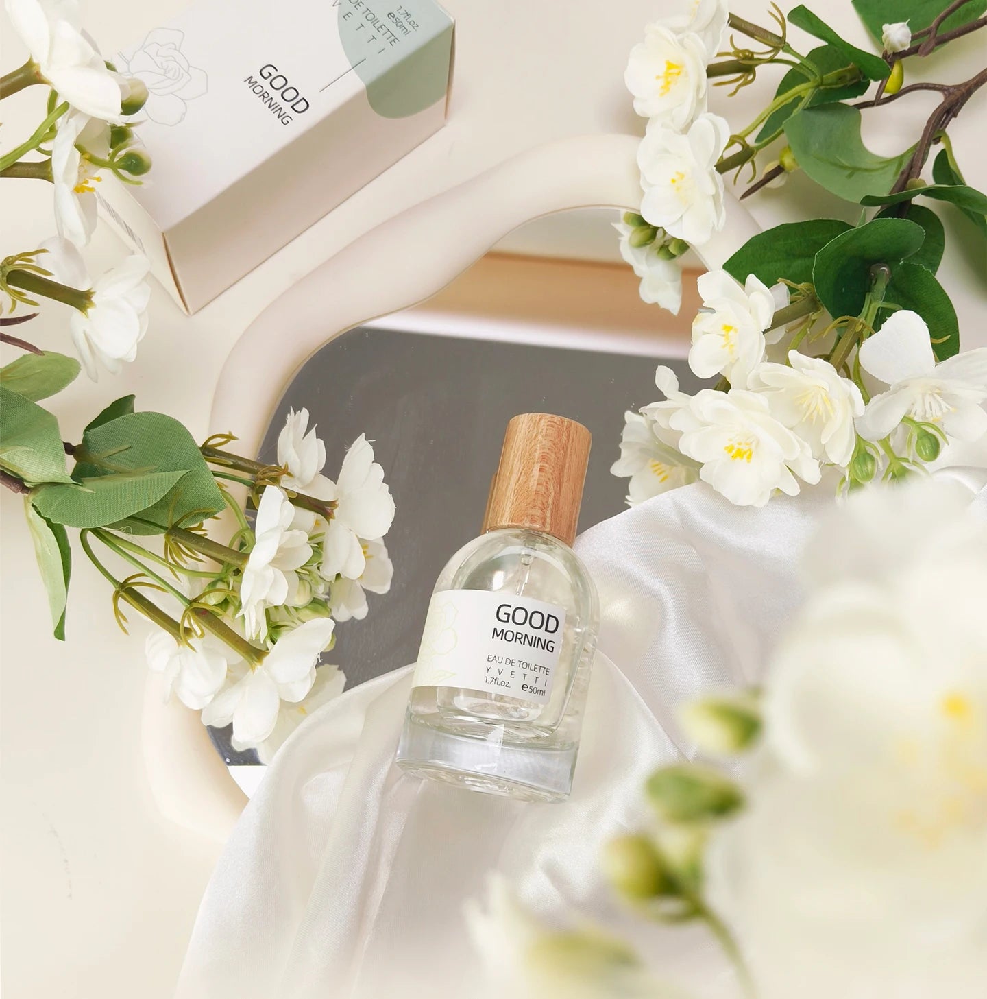 Elegant Good Morning niche gardenia perfume with a wood-cap glass bottle on a white satin cloth and floral background.